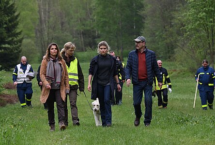 "Erzgebirgskrimi - Familienband": Ein Suchtrupp läuft eine Wiese ab. Im Vordergrund stehen Mutter Corinna Ott (Katharina Wackernagel), Försterin Saskia Bergelt (Teresa Weißbach) mit Hund Wolke, Kommissarin Karina Szabo (Lara Mandoki) und Onkel Ralph Ott (Götz Schubert). Im Hintergrund sind Suchhelfer in Warnbekleidung zu sehen.