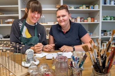 Unter Anleitung von Holzspielzeugmacherin Marie-Theres Langer (r.), die im Betrieb für die Ausbildung zuständig ist,bemalt Maria Hansen Schuhe für die Miniaturfigur Aschenbrödel. Foto: Kristian Hahn